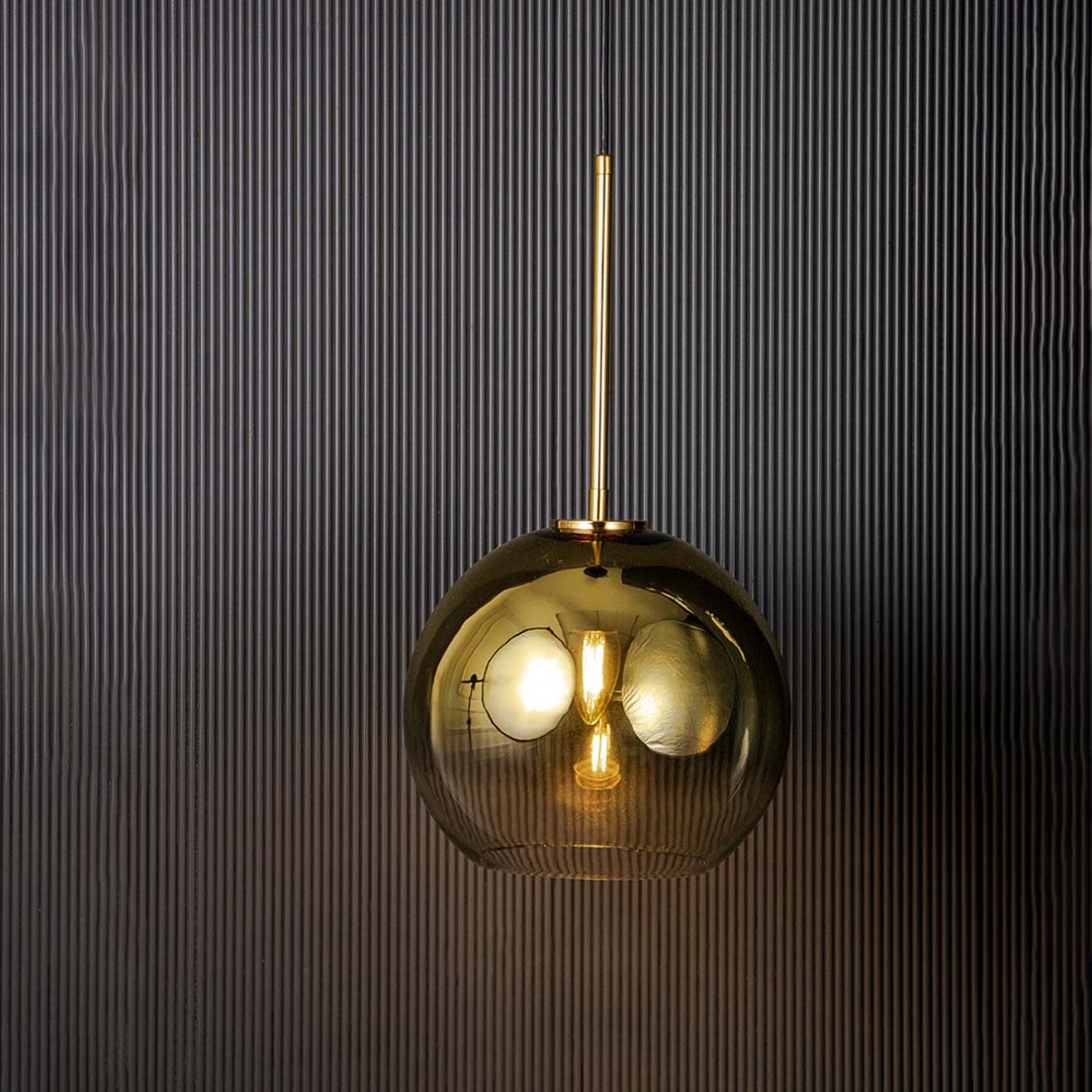 Light on black background showing a modern gold pendant light with smoked glass shade and warm glowing bulb highlighting the sleek metal finish and contemporary design.