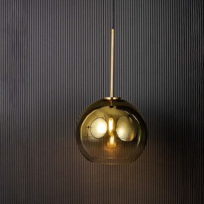 Light on black background showing a modern gold pendant light with smoked glass shade and warm glowing bulb highlighting the sleek metal finish and contemporary design.