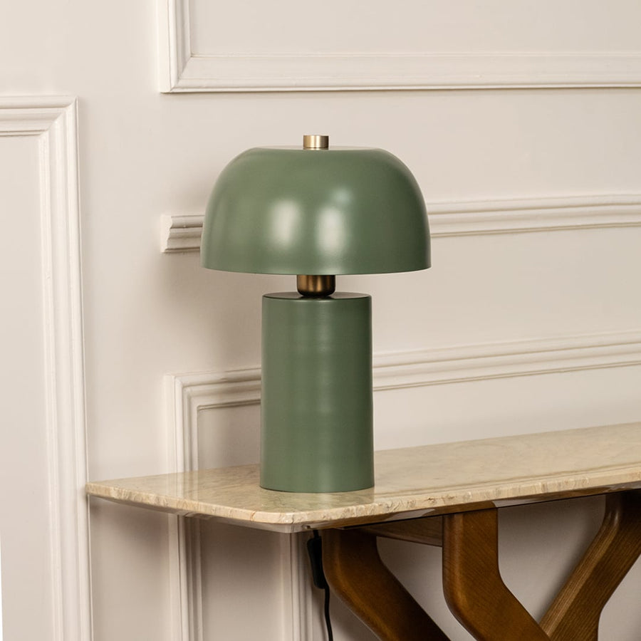 Green dome shade metal table lamp on marble shelf with light off for modern minimalist décor.