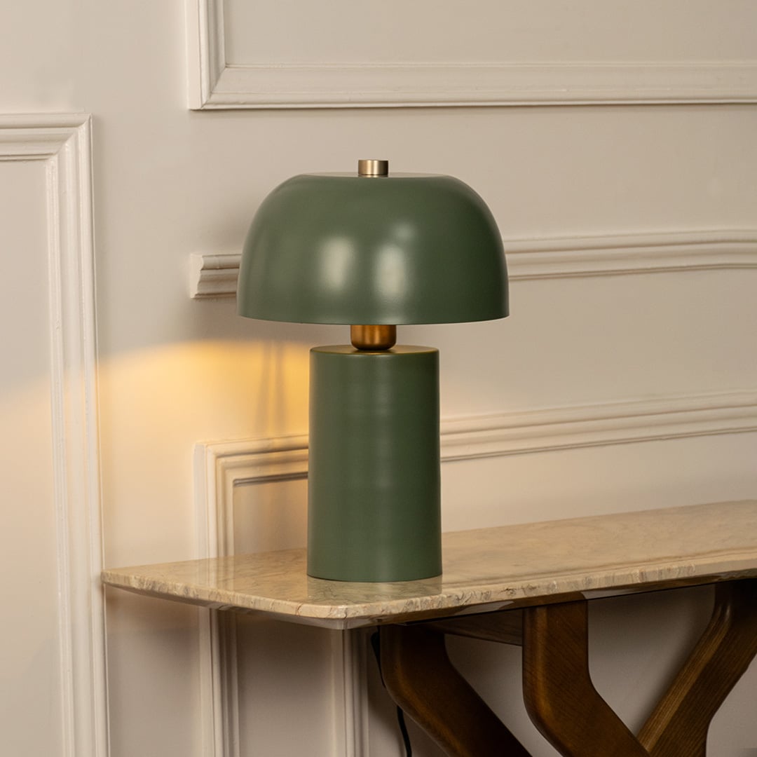 Green dome shade metal table lamp on marble shelf with light on for modern minimalist décor.