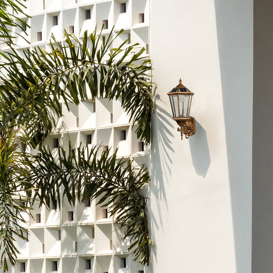 Outdoor antique gold wall lantern mounted on a light background showcasing its classic shape clear glass panels and elegant vintage design.
