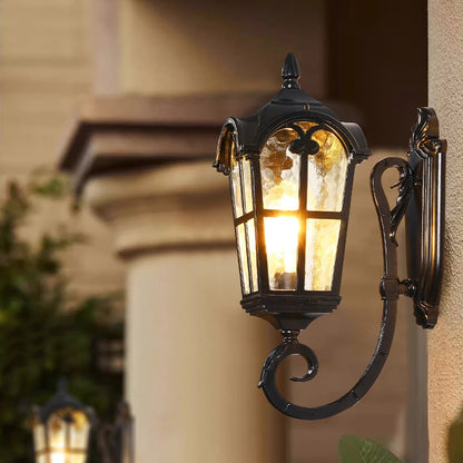 Black metal outdoor wall light lifestyle image with textured glass shade glowing on an exterior house wall for decor.
