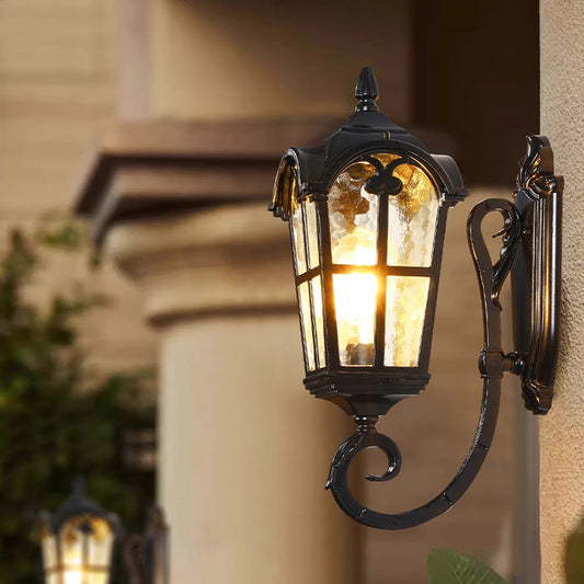 Black metal outdoor wall light lifestyle image with textured glass shade glowing on an exterior house wall for decor.