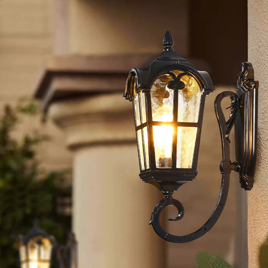 Black metal outdoor wall light lifestyle image with textured glass shade glowing on an exterior house wall for decor.