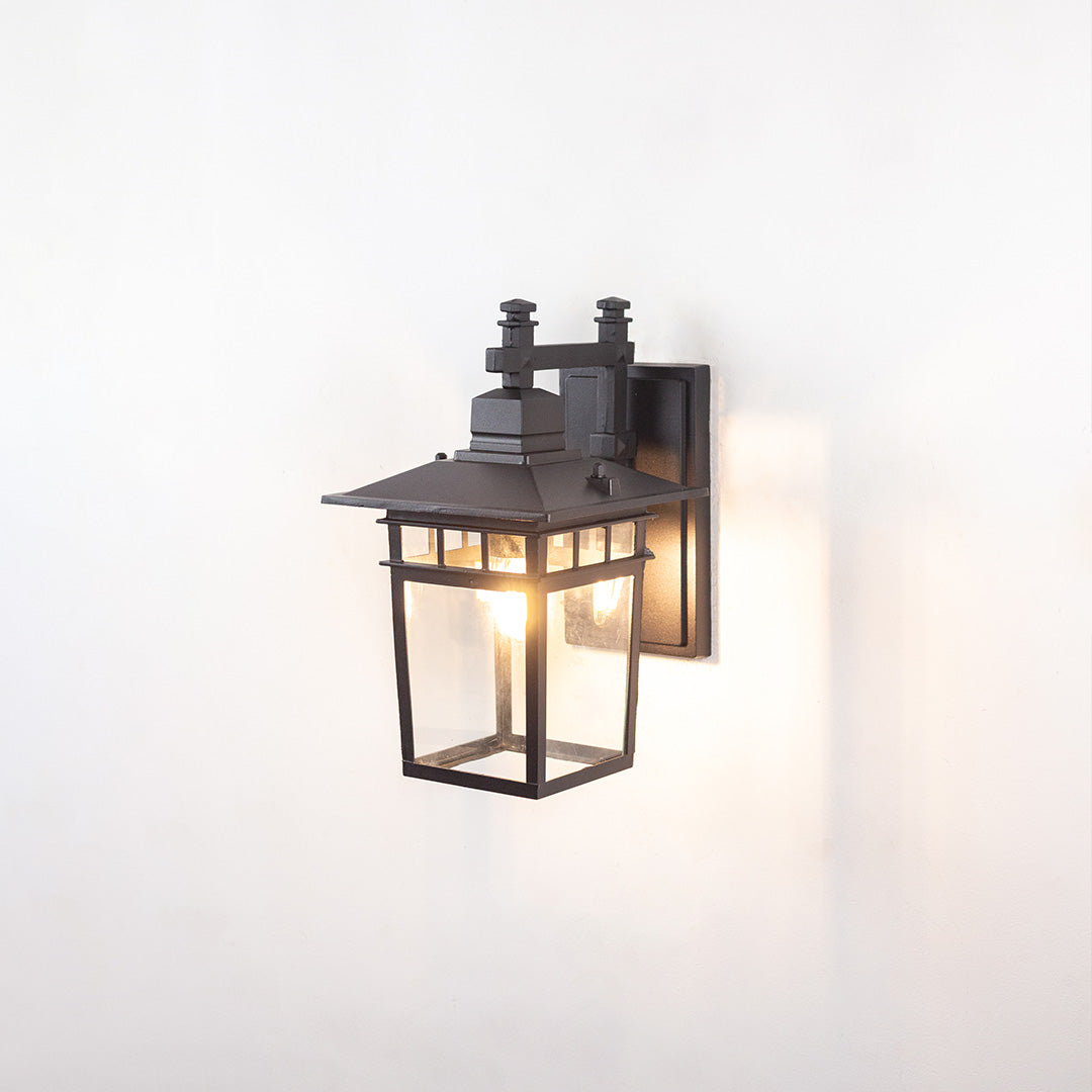 Black metal outdoor wall light on white background with clear glass panels and craftsman style frame for patio decor.