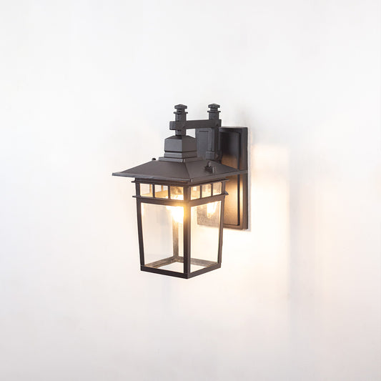 Black metal outdoor wall light on white background with clear glass panels and craftsman style frame for patio decor.