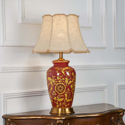Red ceramic floral table lamp with gold detailing and a beige fabric shade adding a warm elegant accent to classic living room and bedroom decor.