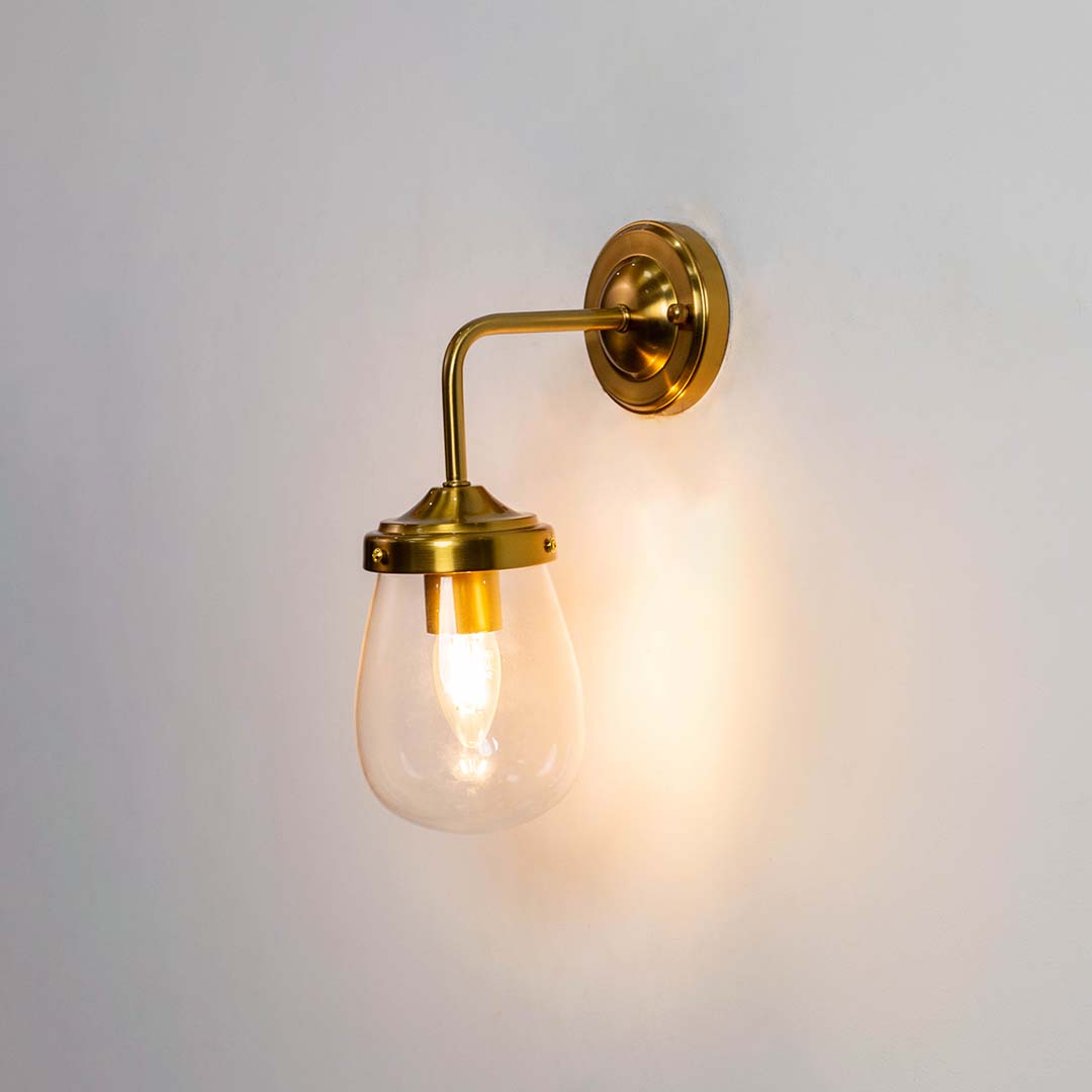 Gold wall sconce with teardrop glass shade shown with the light on against a clean white background creating a warm and inviting glow.