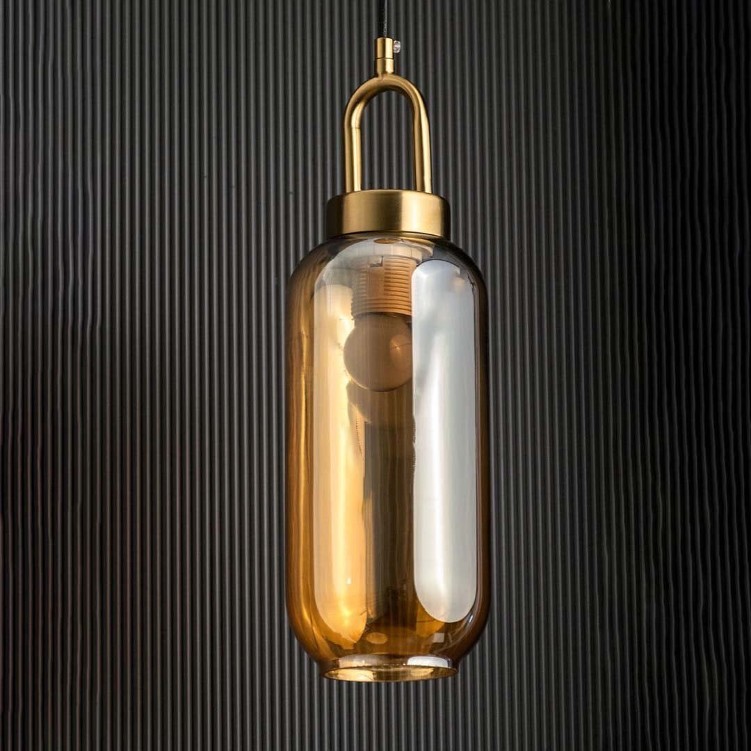 A gold and amber glass pendant light with lights off against a dark textured background emphasizing its tall cylindrical amber glass and gold top detail.