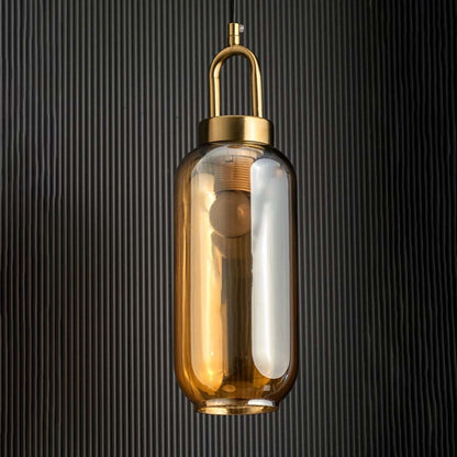 A gold and amber glass pendant light with lights off against a dark textured background emphasizing its tall cylindrical amber glass and gold top detail.