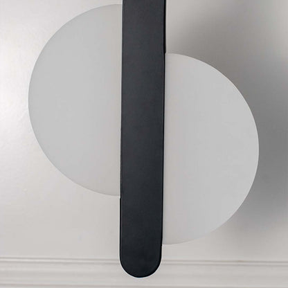 Closeup modern wall light with white circular backplate and black vertical bar placed against neutral wall background showcasing minimal lighting decor styling.