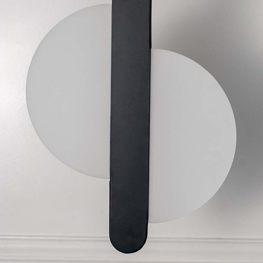 Closeup modern wall light with white circular backplate and black vertical bar placed against neutral wall background showcasing minimal lighting decor styling.