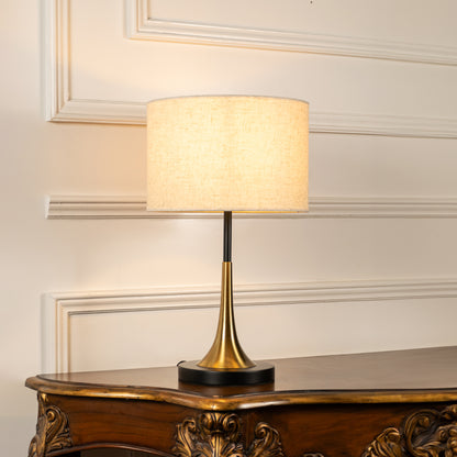 Brass metal table lamp with fabric drum shade displayed on a carved wooden console table creating elegant ambient lighting.