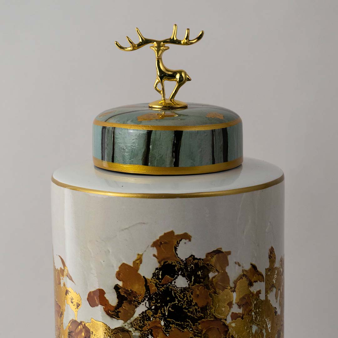 White ceramic jar with deer lid and botanical artwork placed on white surface against neutral background showcasing luxury decorative home decor styling.