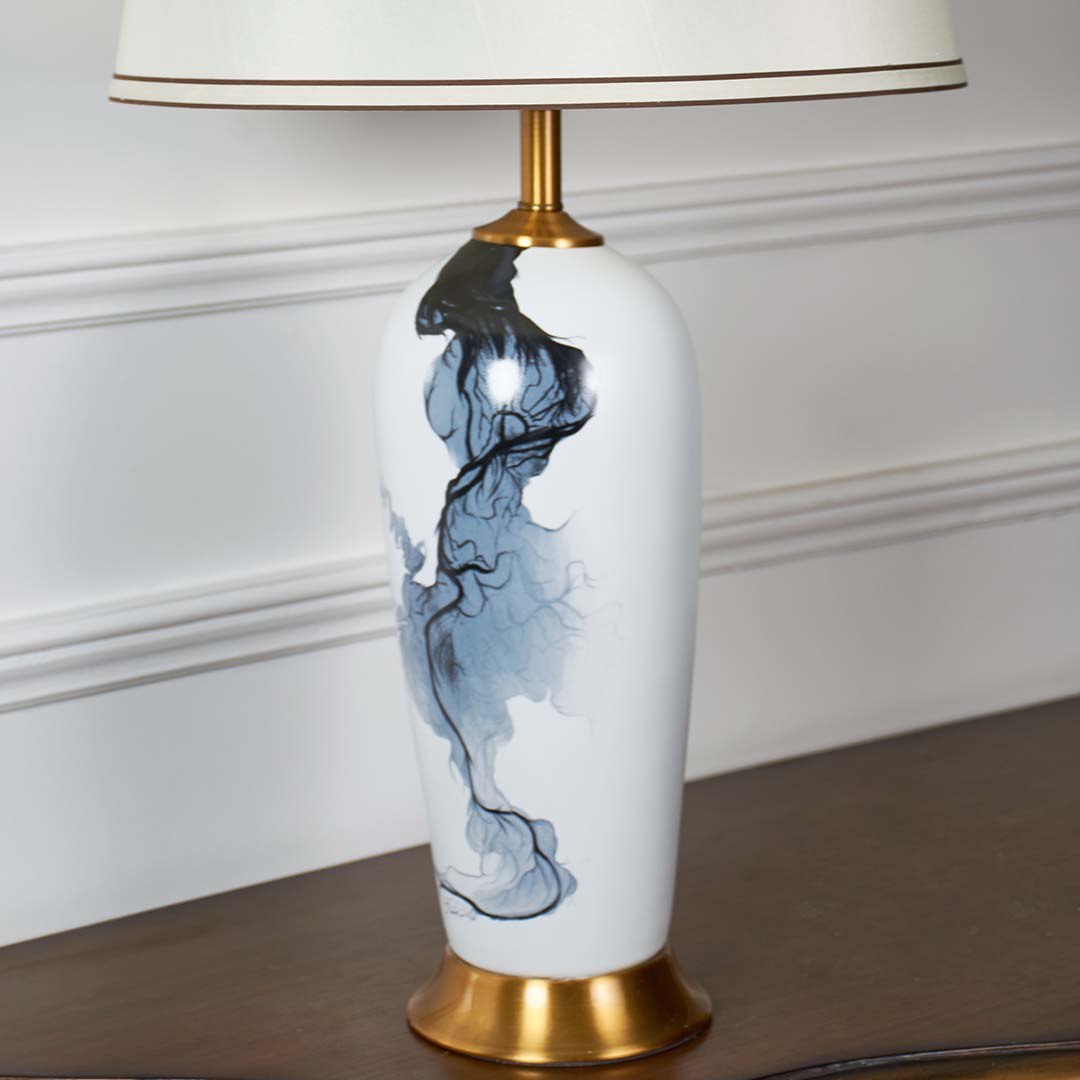 Closeup of white ceramic lamp with flowing blue abstract artwork gold base and cream shade showcasing refined craftsmanship and modern elegance.