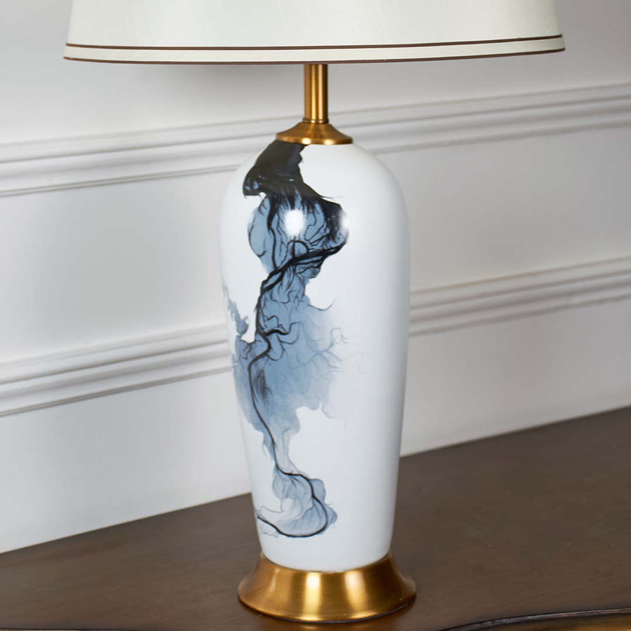 Closeup of white ceramic lamp with flowing blue abstract artwork gold base and cream shade showcasing refined craftsmanship and modern elegance.