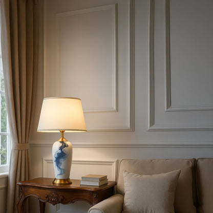 White ceramic table lamp with gold base and cream shade placed on a carved wooden side table adding a soft elegant glow to a classic living room setting.