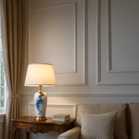 White ceramic table lamp with gold base and cream shade placed on a carved wooden side table adding a soft elegant glow to a classic living room setting.