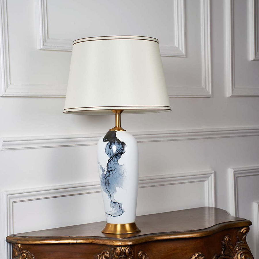 White ceramic lamp with blue abstract pattern gold base and cream shade displayed unlit on a clean white background for premium decor presentation.