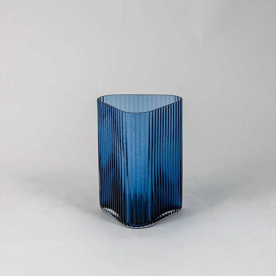 Elegant blue glass vase with fine ribbed texture and soft curves photographed on plain white surface for minimal presentation.