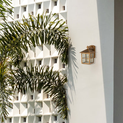 Gold metal outdoor wall lantern with clear window pane glass mounted on a bright white exterior wall creating a warm inviting architectural lifestyle ambience.