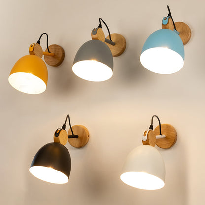 Five colorful dome wall lamps including yellow grey blue black and white variants casting warm light on a plain wall.