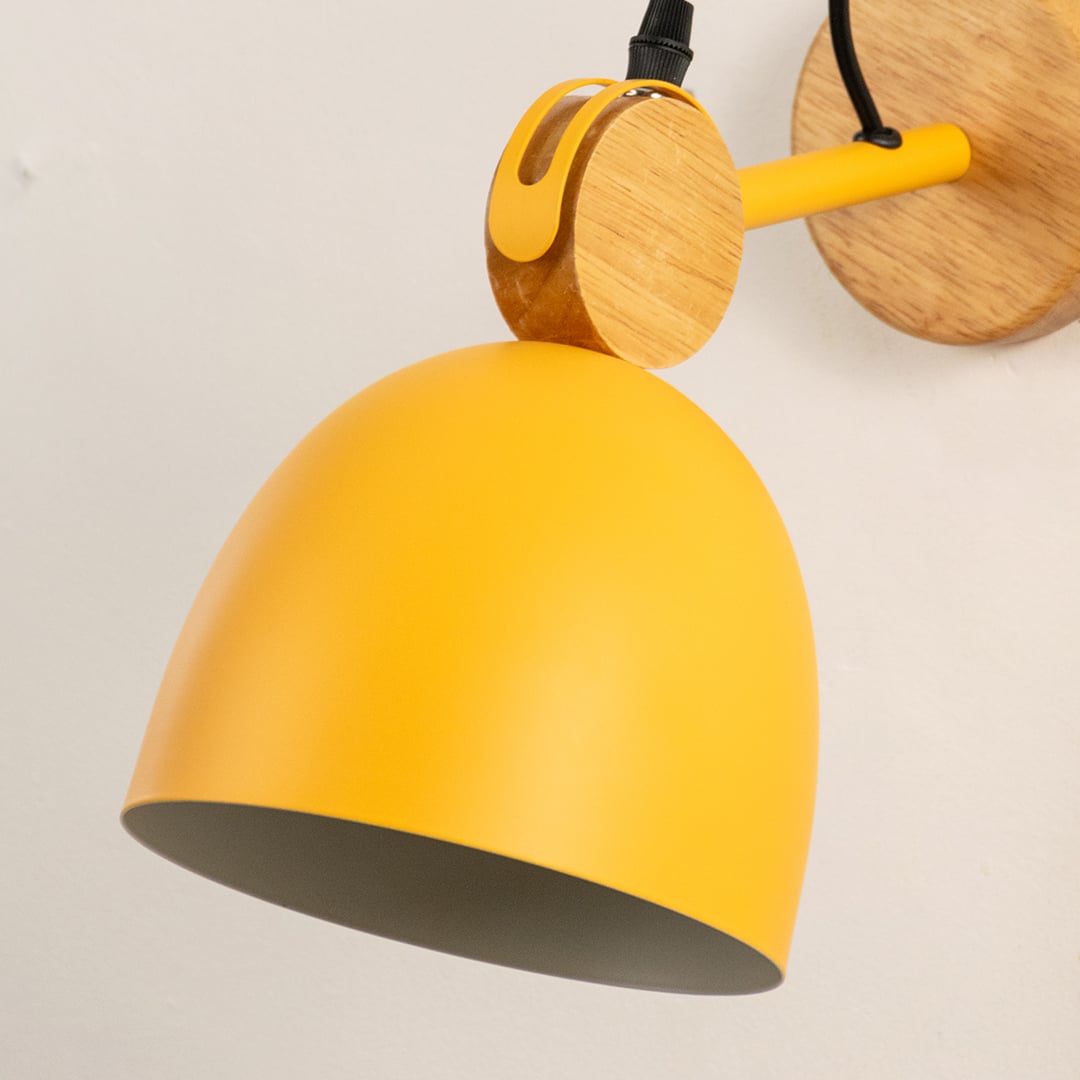 Detailed macro shot of a yellow dome wall lamp focusing on the natural wood swivel hinge assembly and matching bracket.