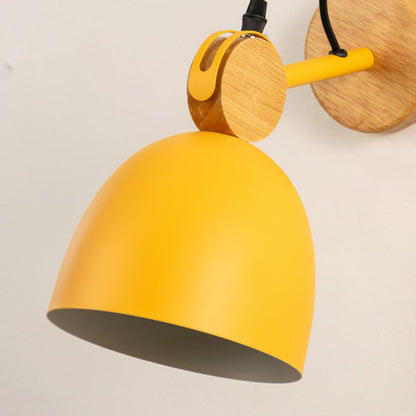 Detailed macro shot of a yellow dome wall lamp focusing on the natural wood swivel hinge assembly and matching bracket.