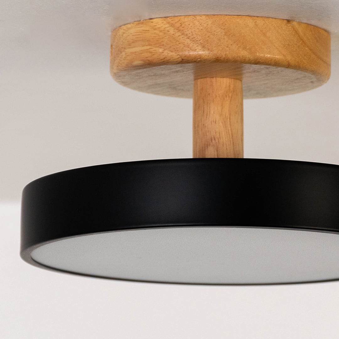Closeup of black metal ceiling light with smooth wood mount highlighting modern finish and warm lighting.