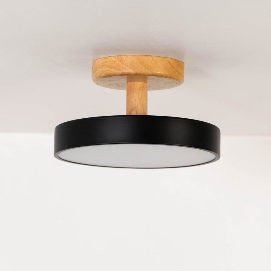 Black metal ceiling light with wood mount displayed on an off white background for clear product detailing.