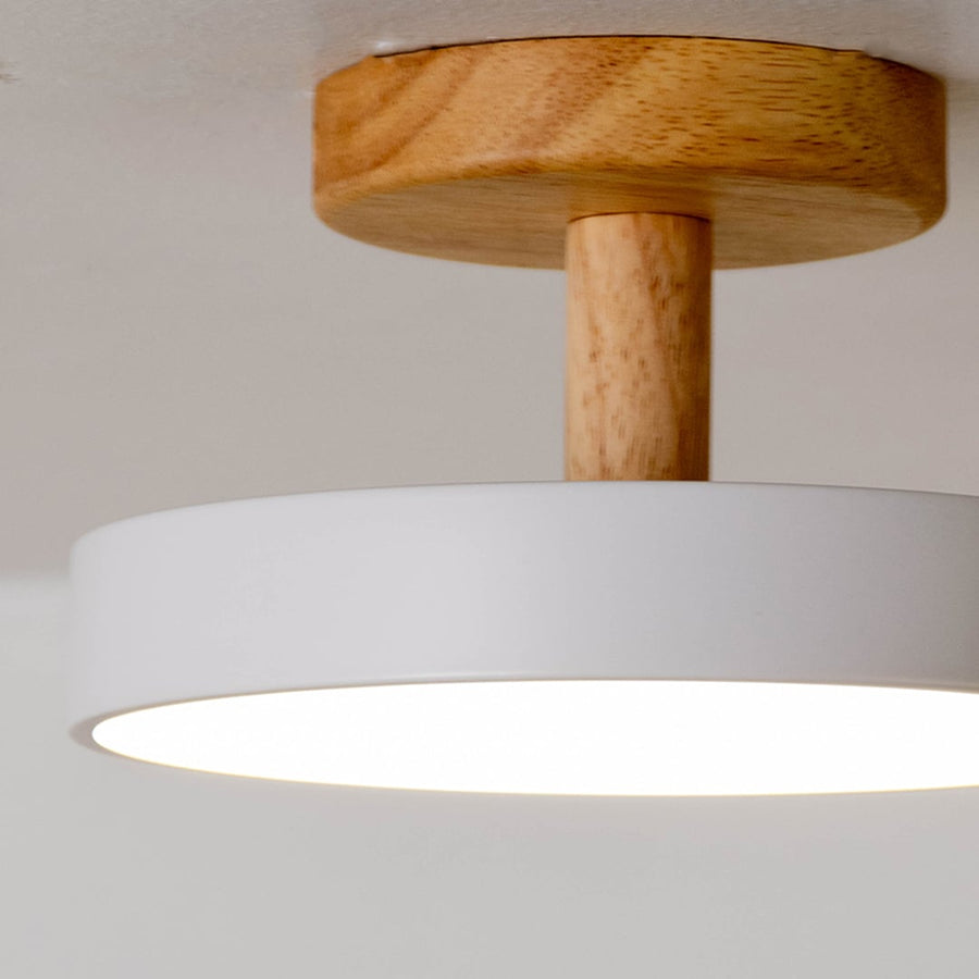 Closeup view of a round ceiling light showing the smooth white shade and natural wooden base with a clean modern finish captured on a bright white background.