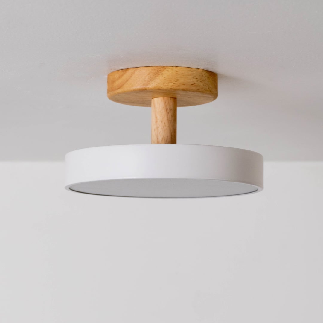 Round ceiling light with the light switched off displayed on a white background highlighting the sleek white shade and wooden mount in a simple minimal design.