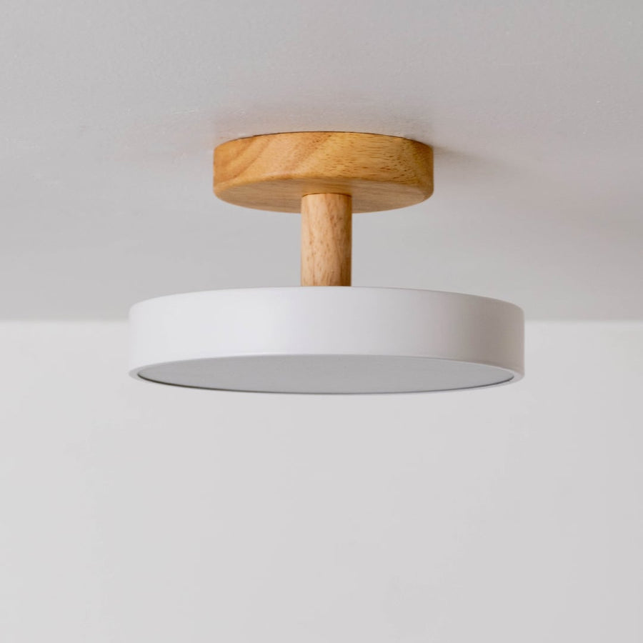 Round ceiling light with the light switched off displayed on a white background highlighting the sleek white shade and wooden mount in a simple minimal design.