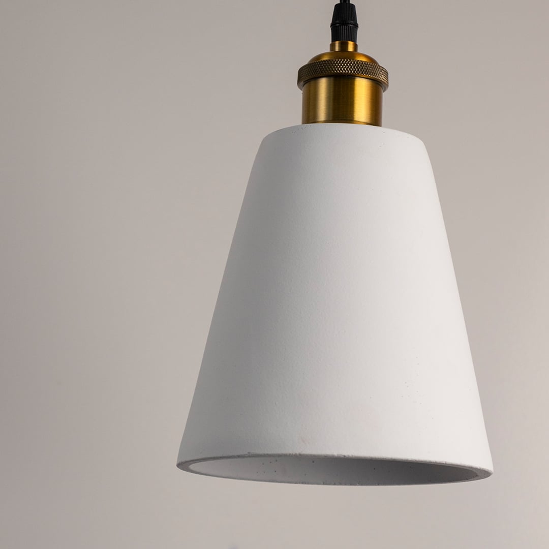 Closeup of white cone pendant lamp emitting warm soft light with elegant matte finish and brass holder.