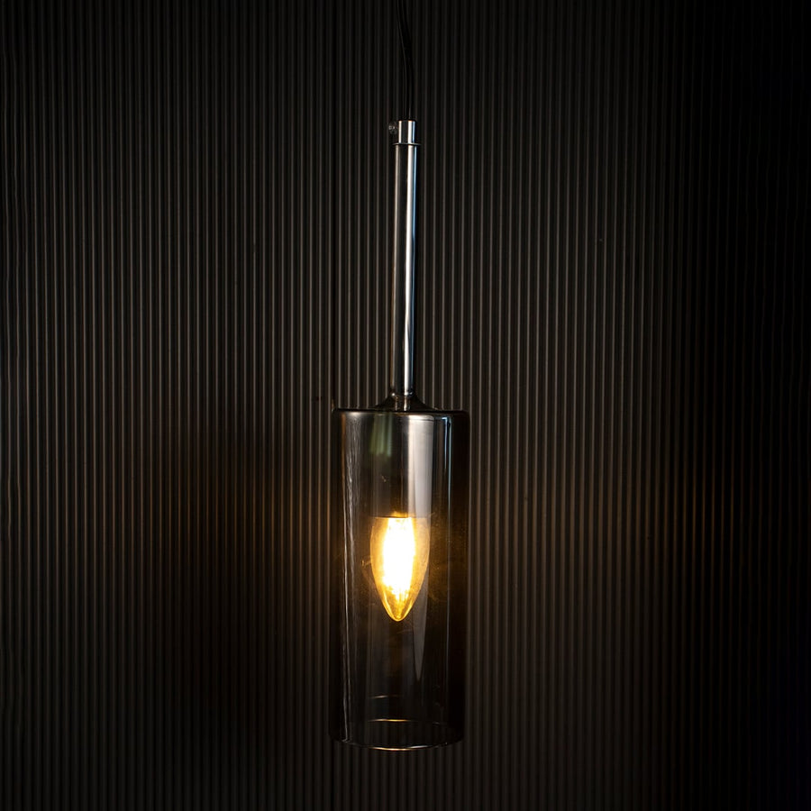 Chrome pendant light glowing warmly against black background emphasizing its refined industrial-inspired design.