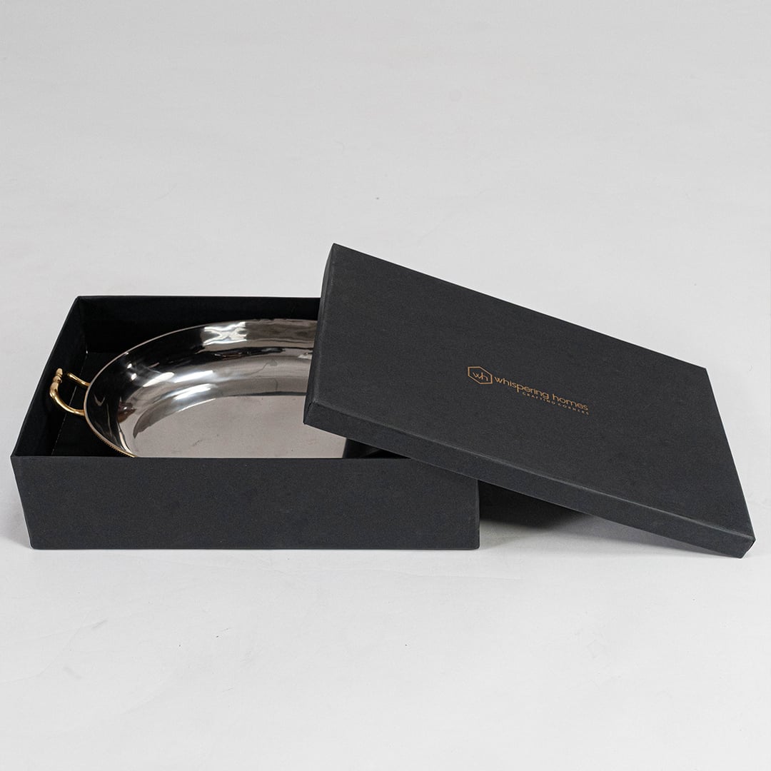Stainless steel decorative tray with gold handles and raised feet shown at angle on plain white background.