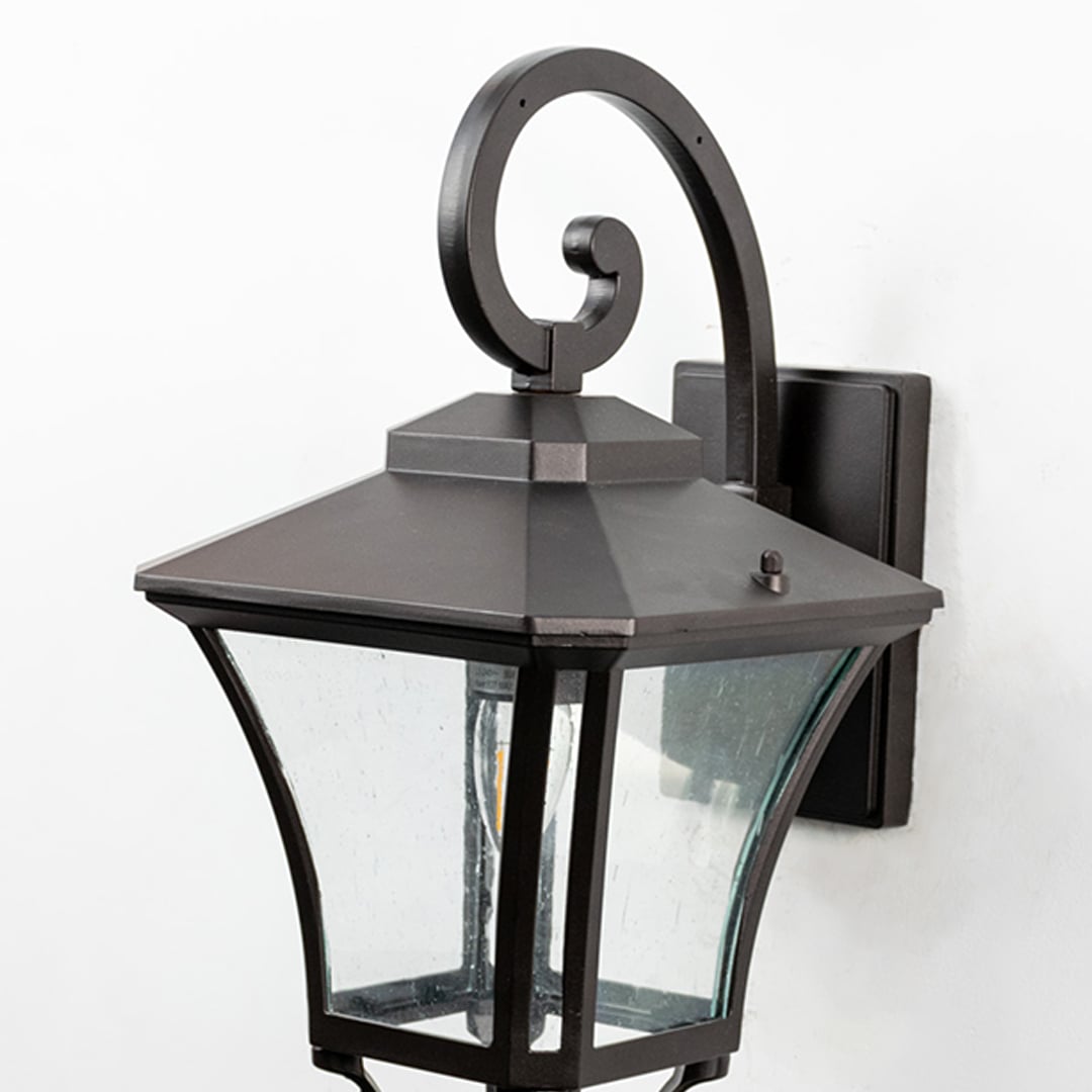Traditional black metal wall lantern closeup focusing on curved arm scrollwork and glass enclosure craftsmanship for outdoor decor.
