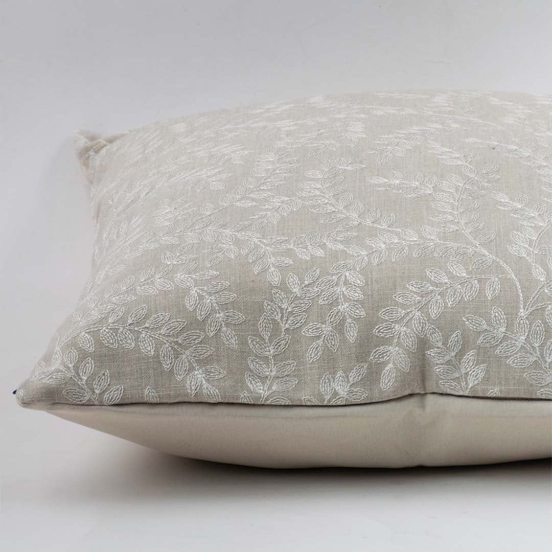 Decorative beige cushion cover with elegant white leaf embroidery on plain white background.