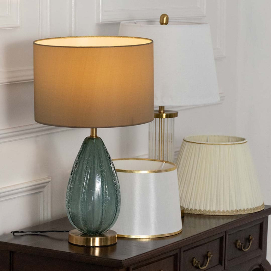 Brown shade blue glass lamp on console table with light on and white wall background for cozy elegant décor.