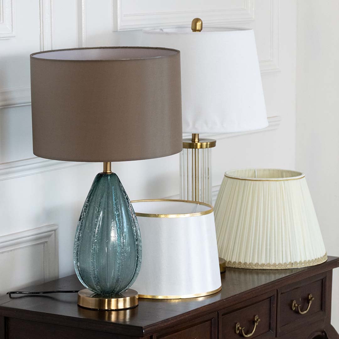 Teal glass table lamp with brown shade on wooden sideboard shown in close up view with light off for stylish contemporary décor.