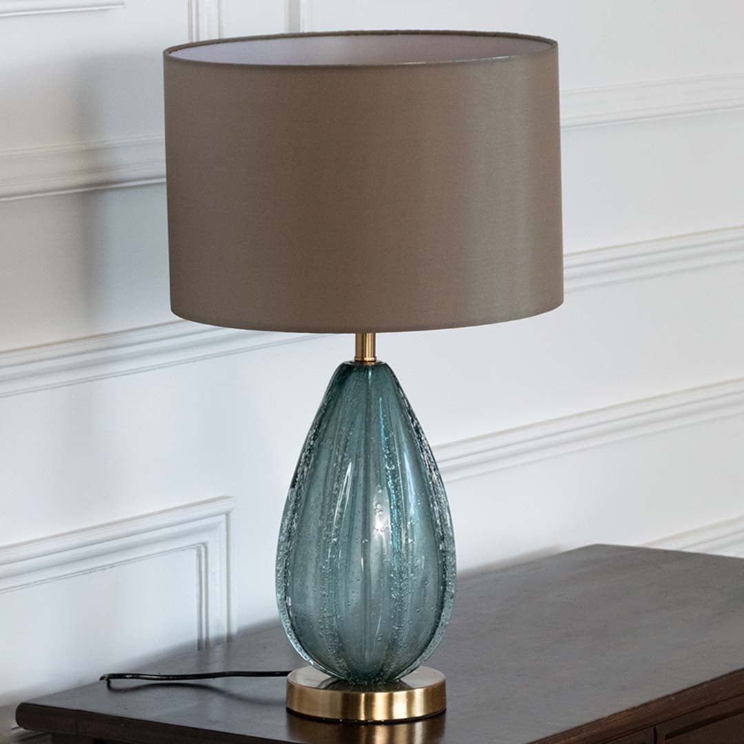 Blue glass lamp with grey shade on console table with light off and white wall background for modern décor.
