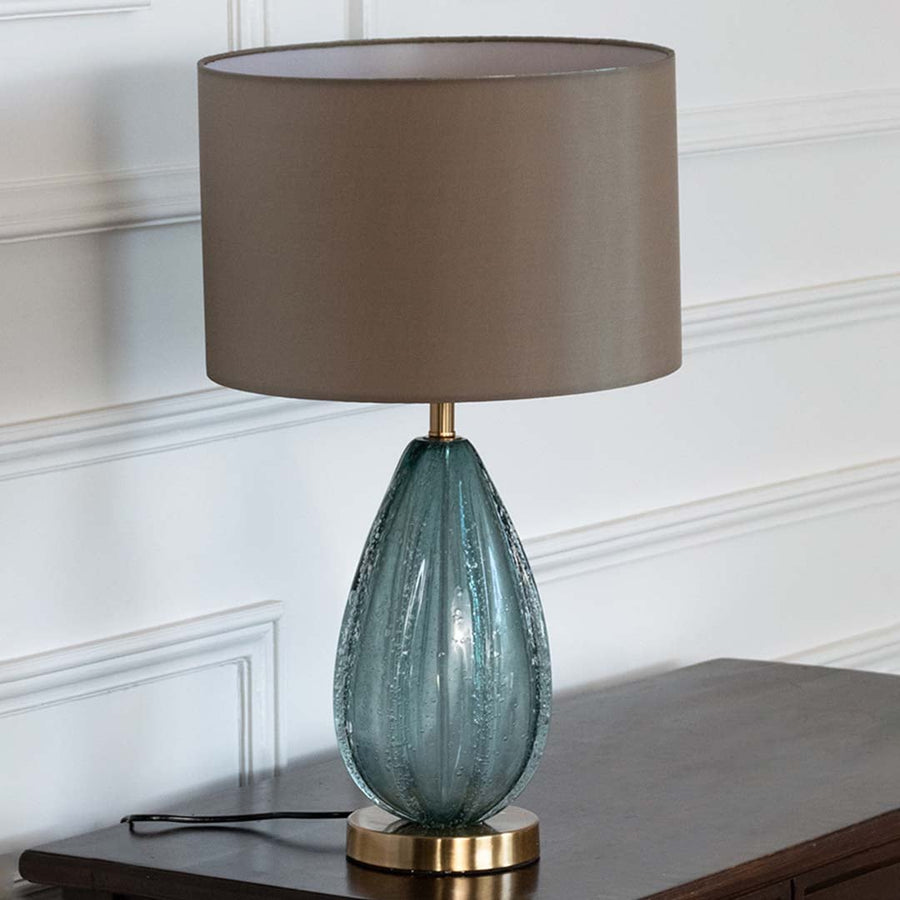 Blue glass lamp with grey shade on console table with light off and white wall background for modern décor.