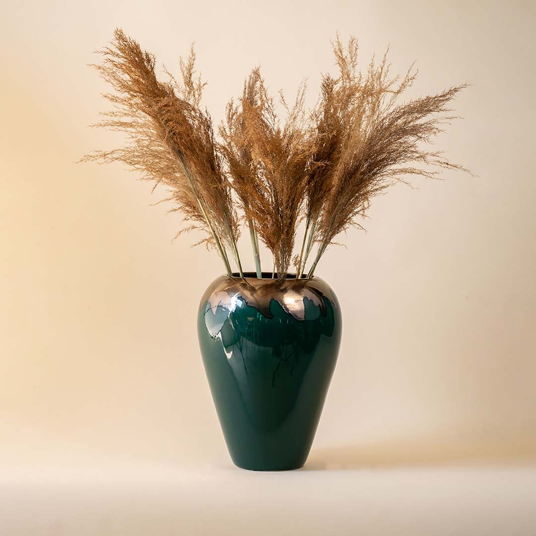 Tall green vase with glossy finish and dried pampas stems styled against a neutral beige backdrop.