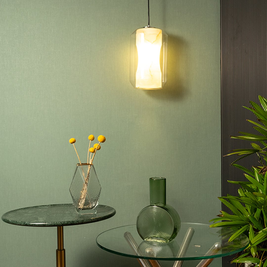 A modern cylindrical pendant light glowing warmly with frosted marble glass and transparent outer shell adding soft ambient lighting to a serene living corner.