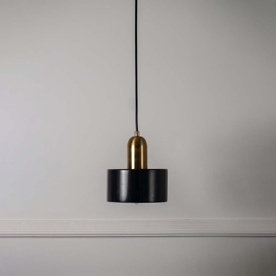 Black and gold pendant ceiling light with sleek cylindrical shape presented against minimal off white background for decor.
