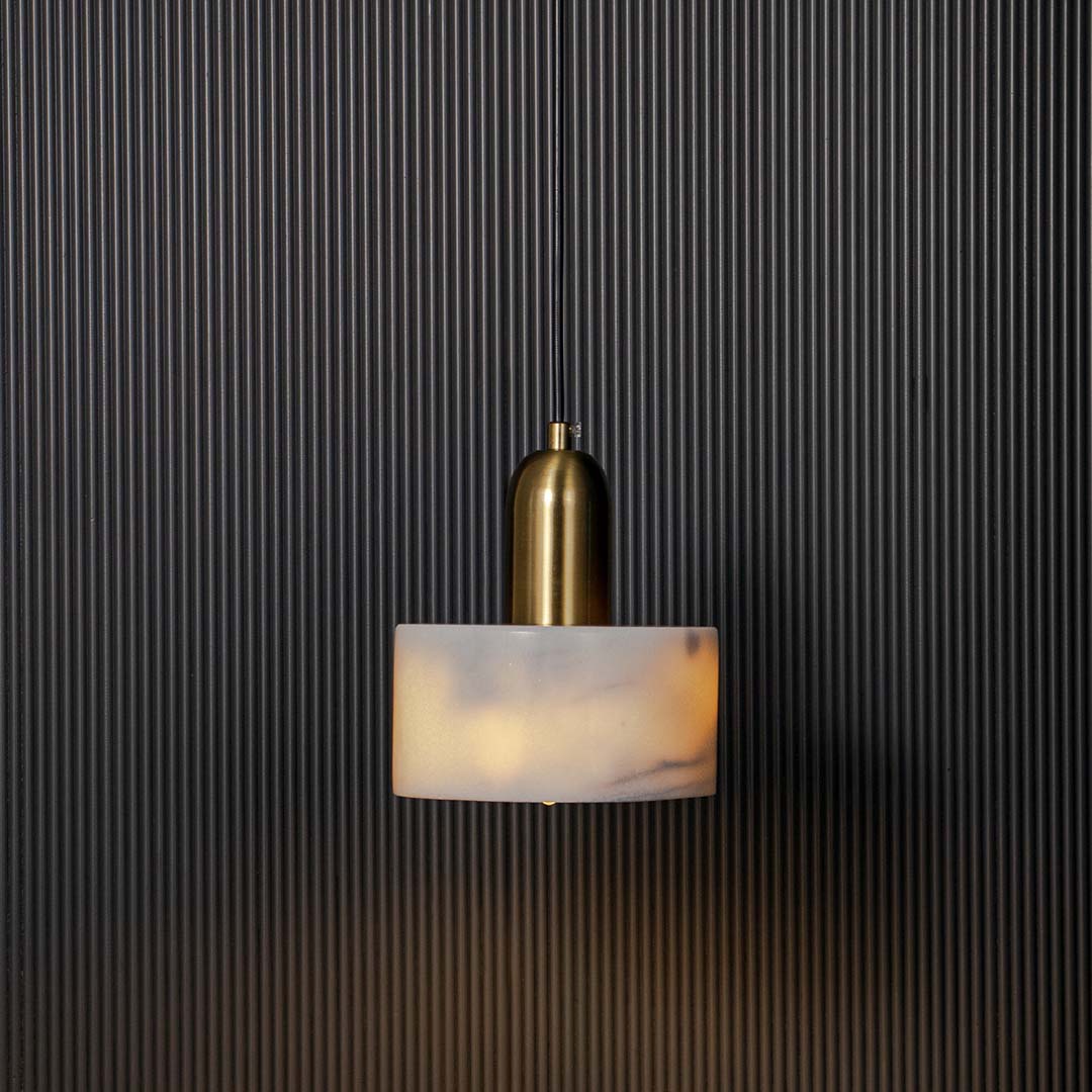 White marble and gold cylindrical pendant ceiling light illuminated beautifully against black background for luxury decor.
