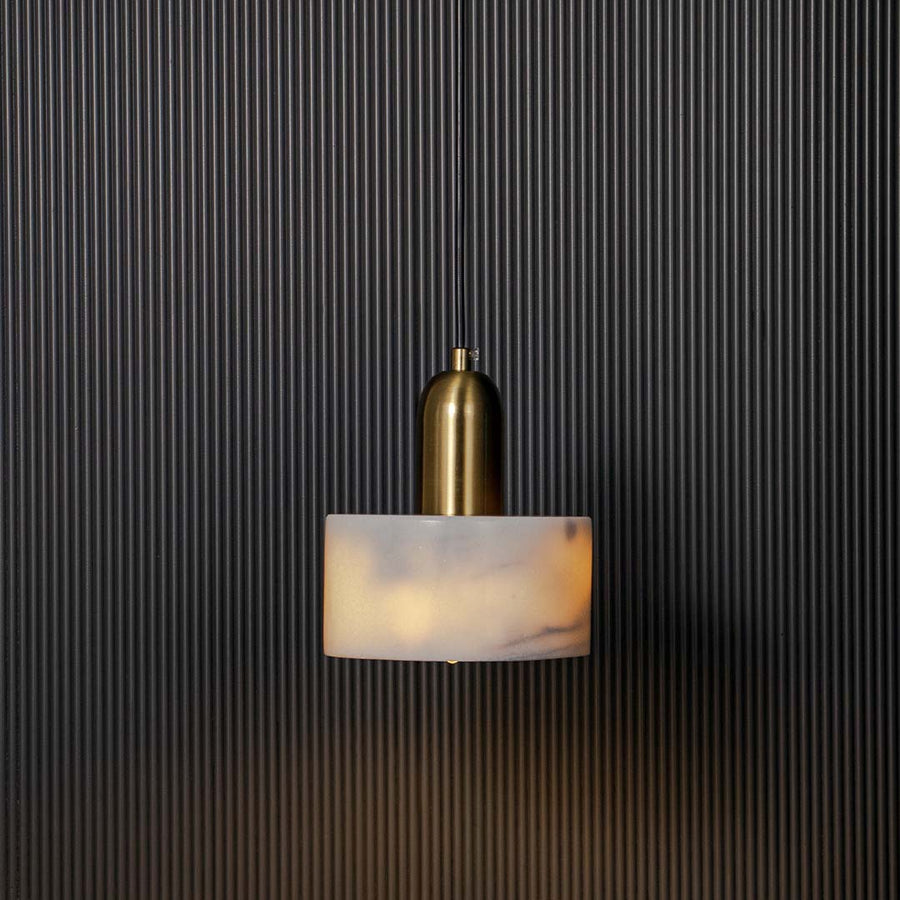 White marble and gold cylindrical pendant ceiling light illuminated beautifully against black background for luxury decor.