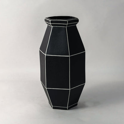 Stylish black geometric ceramic vase with angular shape and white line detailing ideal for living room or office decor.