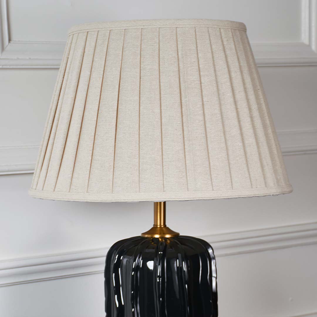 White pleated fabric shade with gold stem detail on black ceramic table lamp showcasing luxury craftsmanship and style.