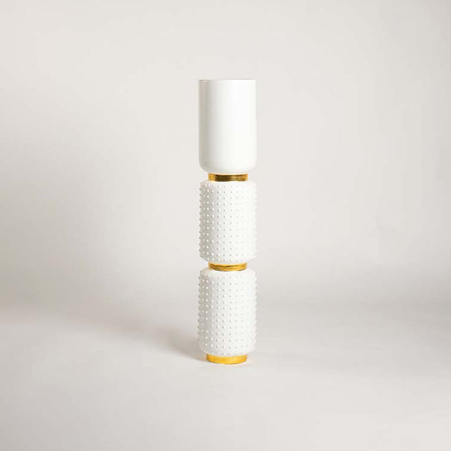 Modern white ceramic and gold vase photographed on a clean white backdrop showing its tall structure smooth top section and textured lower cylinders.